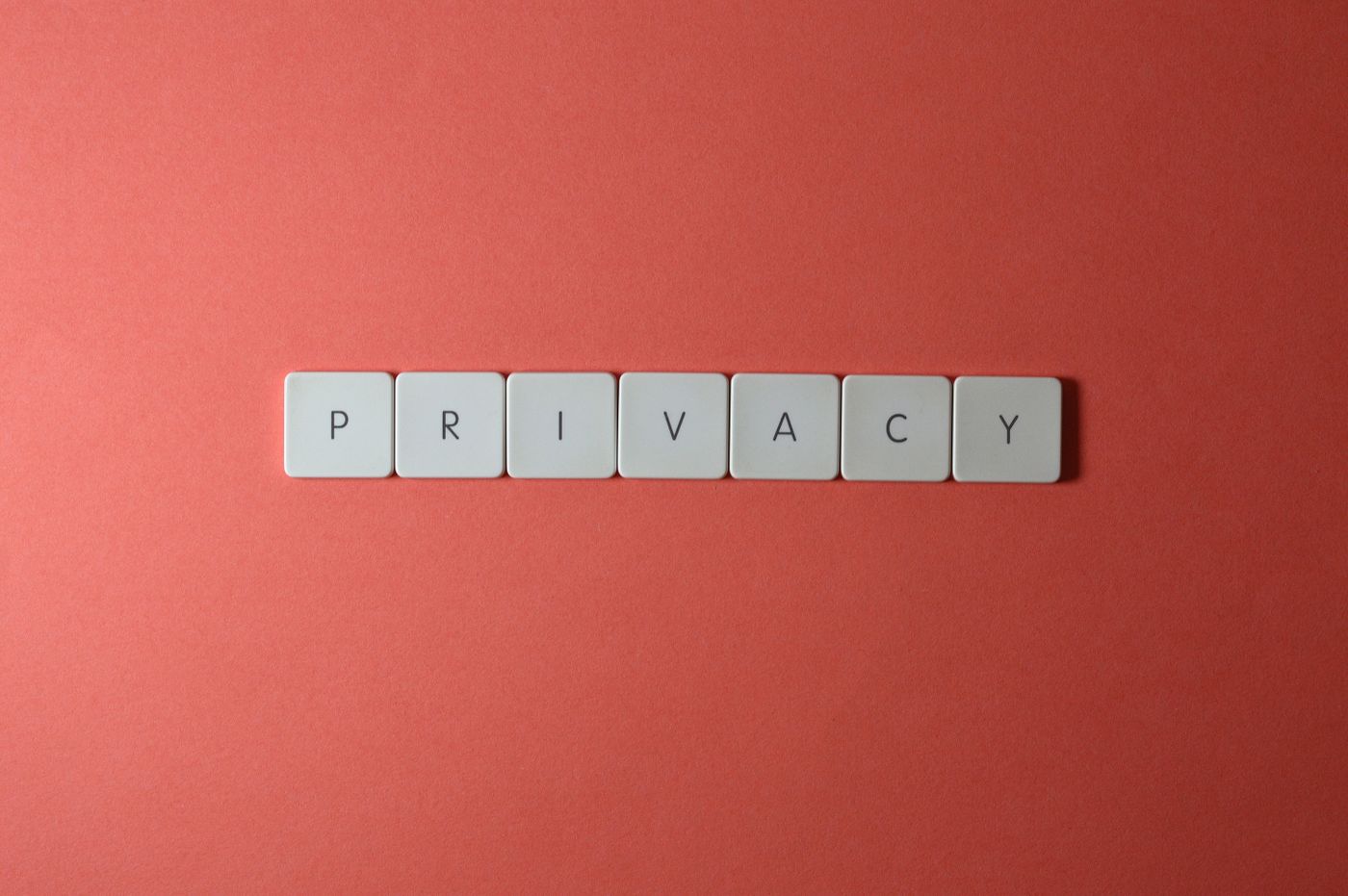 Seven white letter tiles arranged on a terracotta background to spell the word PRIVACY